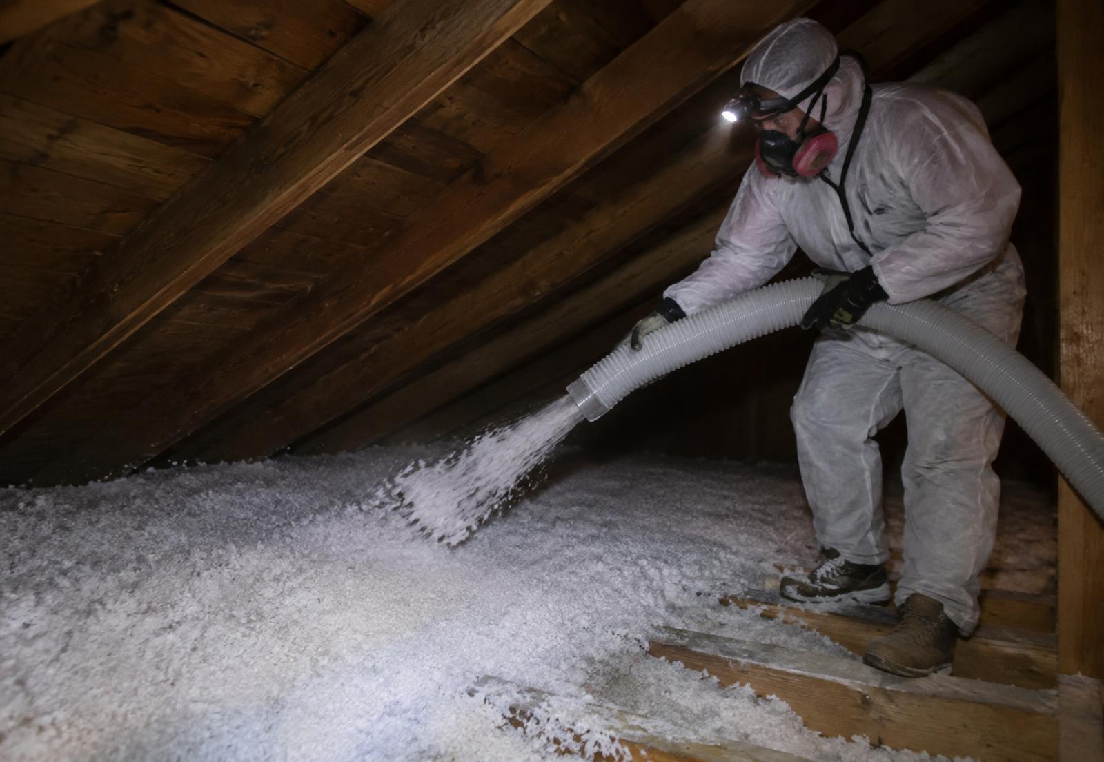Technicien soufflant de l'isolant en fibre de verre sur le plancher d'un entretoit